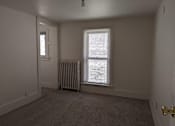 Thumbnail 23 of 29 - A room with a carpeted floor, a window with blinds, a door, and a radiator.