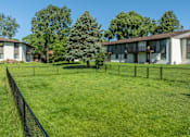 Thumbnail 15 of 20 - A grassy field with a fence and apartment buildings in the background.