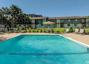 Thumbnail 17 of 20 - A large swimming pool in front of a building with a lawn and trees in the background.
