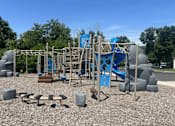 Thumbnail 10 of 15 - A playground with a blue slide and grey and brown play equipment.