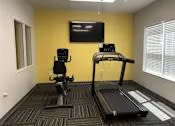 Thumbnail 3 of 15 - A gym room with a treadmill, a stationary bike, and a television.