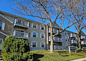 Thumbnail 1 of 11 - A large grey apartment building with a balcony on the second floor.