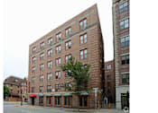 Thumbnail 23 of 25 - A tall red brick building with many windows stands on a street corner.
