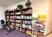 Thumbnail 10 of 14 - A room with a bookshelf full of books and a chair with a plant on top.