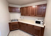 Thumbnail 11 of 14 - A kitchen with brown cabinets and a white microwave.