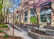 Thumbnail 1 of 31 - A walkway with red railings and trees in front of a building.