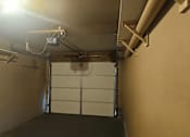 Thumbnail 15 of 16 - A garage with a white door and a light on the ceiling.