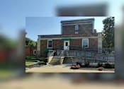 Thumbnail 2 of 4 - A brick building with a green door and steps leading up to it.