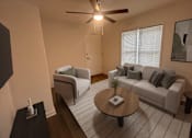 Thumbnail 3 of 20 - A living room with a grey couch, a coffee table, and a ceiling fan.