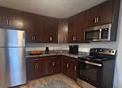 Thumbnail 16 of 20 - A kitchen with a stainless steel refrigerator, black oven, and wooden cabinets.
