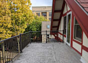 Thumbnail 14 of 29 - A balcony with a black railing and a red and white building in the background.