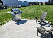 Thumbnail 20 of 21 - A BBQ grill is on a patio with two chairs.