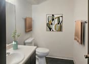 Thumbnail 5 of 7 - A bathroom with a toilet, sink, and a painting on the wall.