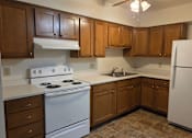 Thumbnail 5 of 14 - A kitchen with white appliances and brown cabinets.