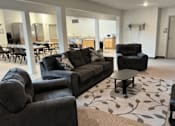 Thumbnail 12 of 15 - A living room with a grey couch and a black armchair.