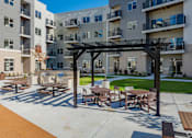 Thumbnail 35 of 80 - A patio with tables and chairs is in front of apartment buildings.