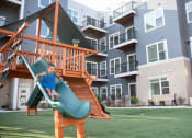 Thumbnail 19 of 39 - a young boy playing on a slide in front of an apartment complex