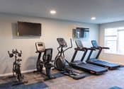 Thumbnail 17 of 39 - a gym with cardio equipment and a tv on the wall