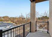 Thumbnail 15 of 80 - A balcony with a black railing and a view of a parking lot and trees.