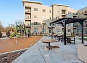 Thumbnail 36 of 80 - A playground area with a slide and picnic tables in front of apartment buildings.
