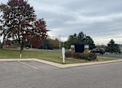 Thumbnail 33 of 36 - A parking lot with a sign and a tree with red leaves.