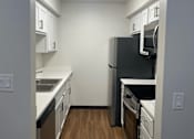 Thumbnail 10 of 36 - A kitchen with a black refrigerator, white cabinets, and a wooden floor.