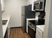 Thumbnail 7 of 36 - A black refrigerator and microwave in a kitchen with white cabinets.