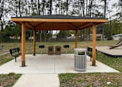 Thumbnail 25 of 36 - A wooden pavilion with a black roof is surrounded by a concrete walkway and a metal trash can.