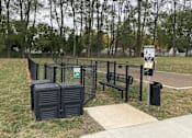 Thumbnail 31 of 36 - A park with a sign, a bench, and a trash can.