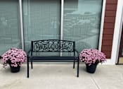 Thumbnail 17 of 36 - A black bench with a flower pot on each side and a sign on the back.