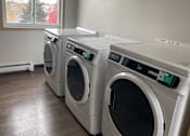 Thumbnail 21 of 36 - Three front load washing machines are lined up in a laundry room.