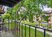 Thumbnail 17 of 25 - A balcony with a black railing and a wooden floor overlooks a green lawn and trees.