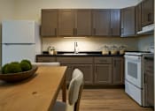 Thumbnail 6 of 21 - A kitchen with a wooden table and chairs, a white refrigerator, and brown cabinets.