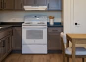 Thumbnail 4 of 21 - A kitchen with a white stove top oven and wooden floors.