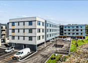 Thumbnail 2 of 21 - A parking lot with a white van and a grey building in the background.