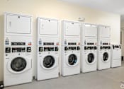 Thumbnail 20 of 21 - A row of white washing machines are lined up against a wall.
