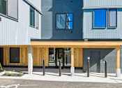 Thumbnail 21 of 21 - A modern building with a grey and blue exterior and a wooden entrance.