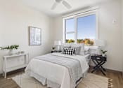 Thumbnail 10 of 21 - A bedroom with a large bed, a ceiling fan, and a window with a view of trees outside.