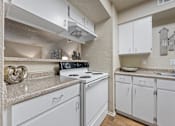 Thumbnail 4 of 38 - White kitchen with electric stove and overhead cabinets at Parks on the Green Apartments, Temple, TX 76504