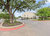 Thumbnail 19 of 38 - Gated property entrance with tree and landscaping at Parks on the Green Apartments, Temple, 76504
