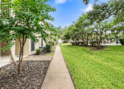 Thumbnail 16 of 38 - Walkway between buildings with mature trees and lawn at Parks on the Green Apartments, Temple, TX