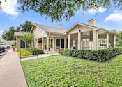 Thumbnail 18 of 38 - Clubhouse building with covered porch and landscaping at Parks on the Green Apartments, Texas