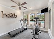 Thumbnail 31 of 38 - Home gym with treadmill and elliptical overlooking pool at Parks on the Green Apartments, Texas