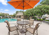Thumbnail 23 of 38 - Pool deck with umbrella table and chairs at Parks on the Green Apartments, Temple, TX