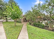 Thumbnail 14 of 38 - Front yard with mature trees and sidewalk at Parks on the Green Apartments, Temple, 76504