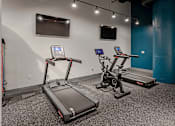 Thumbnail 15 of 18 - Two treadmills are in a room with a blue wall and a television.