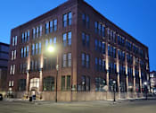 Thumbnail 2 of 14 - A large red brick building with many windows is lit up by a street lamp.