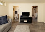 Thumbnail 29 of 36 - A living room with a grey couch and a black television.