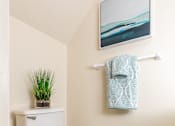 Thumbnail 13 of 31 - A white toilet with a plant on top of the tank and a towel rack with a towel hanging on it.