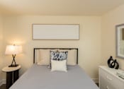 Thumbnail 19 of 26 - A bedroom with a bed, nightstand, lamp, and a blanket.